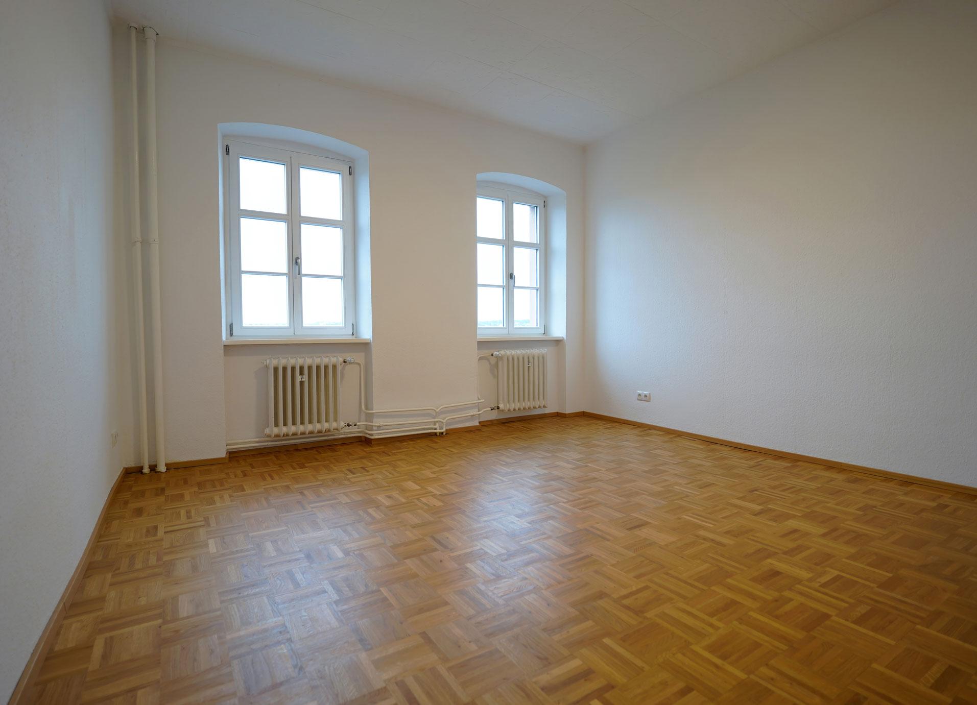 Helles Zimmer mit Parkett und großen Fenstern